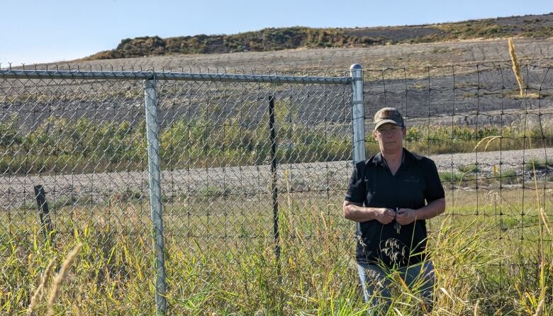 A woman stands in front of a landfill fence