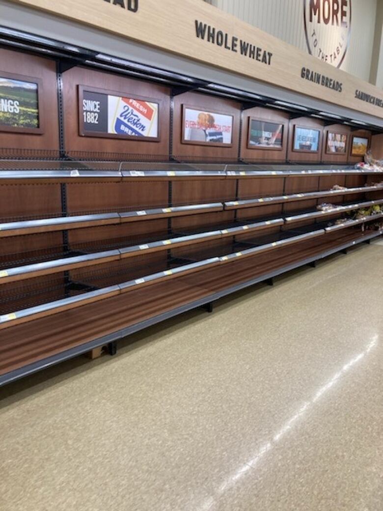 Five shelves in a grocery store bread section are almost completely bare, save for a few bags of buns.