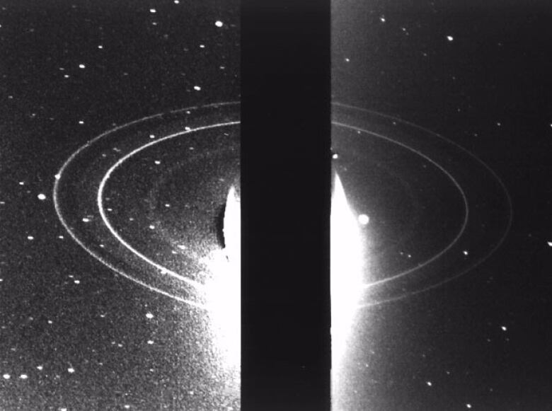 A black and white photo, with a thick black stripe down the center covering something that appears to be a bright white ball. Several rings are circling the bright white ball. 