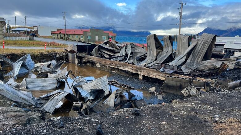 Rubble from a destroyed building is seen with other buildings and a lake in the background.