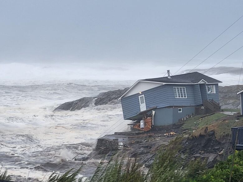 A wide shot of the home in the process of falling into an angry ocean.