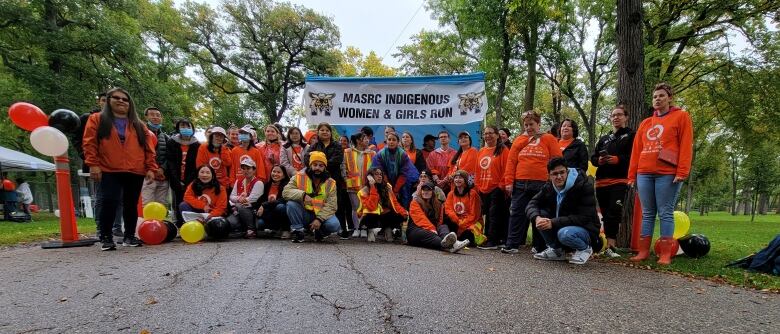 A large group of people in orange T-shirts pose together near a banner that says 'MASRC Indigenous women and girls run.