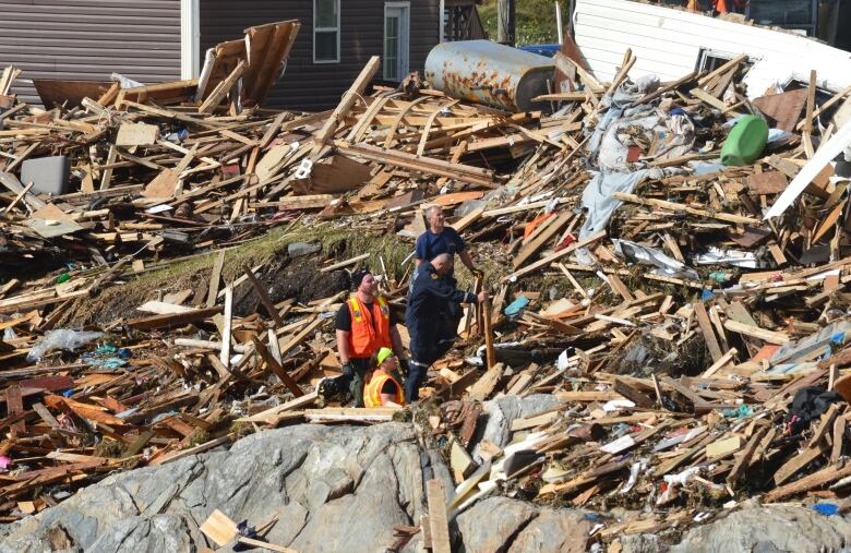 A wide shot of three people standing in the middle of debris.