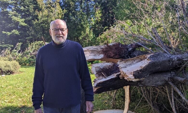 A man stands beside a large tree trunk snapped in half. 