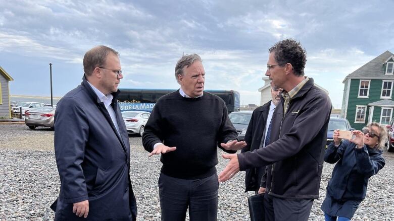 3 men standing outside in a parking lot and talking