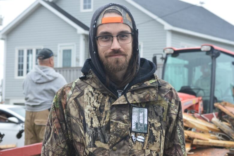 A man in a hunting jacket stands in front of debris.