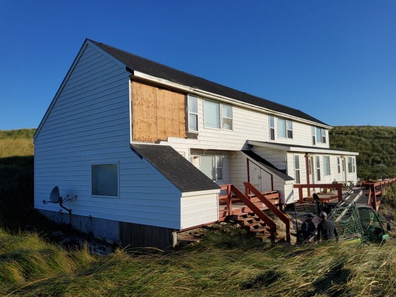 A white building has some siding missing, with plywood showing underneath.