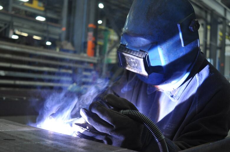 A man with a mask works with a welding torch. 