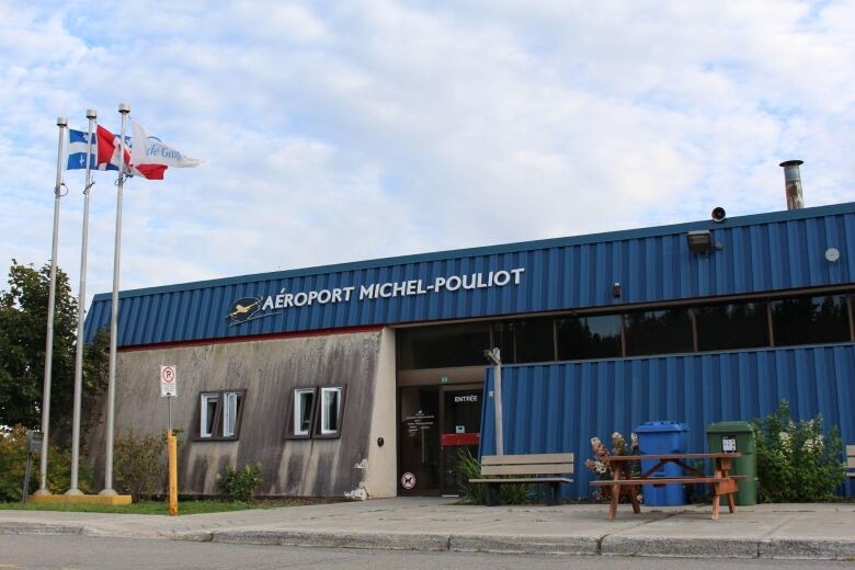 Three flags are seen next to a blue and grey airport building. 