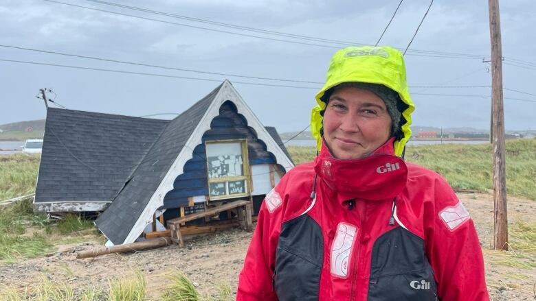 A woman in rain gear stands in front of the debris of a family cottage.