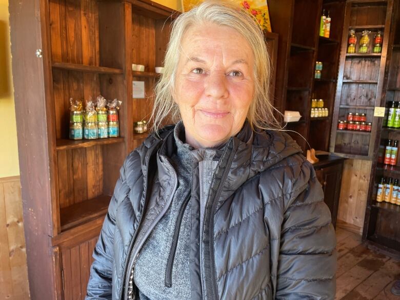 A woman with blond hair stands in front of half-empty shelves in her herb store in the Magdalen Islands