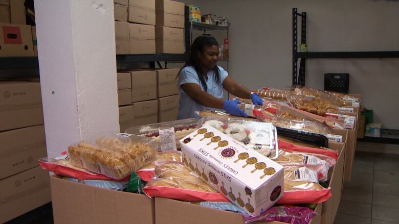 a woman loads food into boxes in a warehouse. 