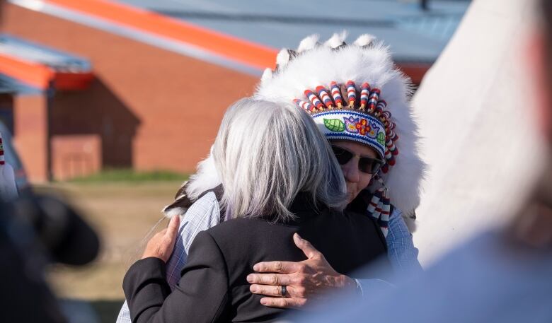 a woman hugs a man who is wearing a Indigenous headdress