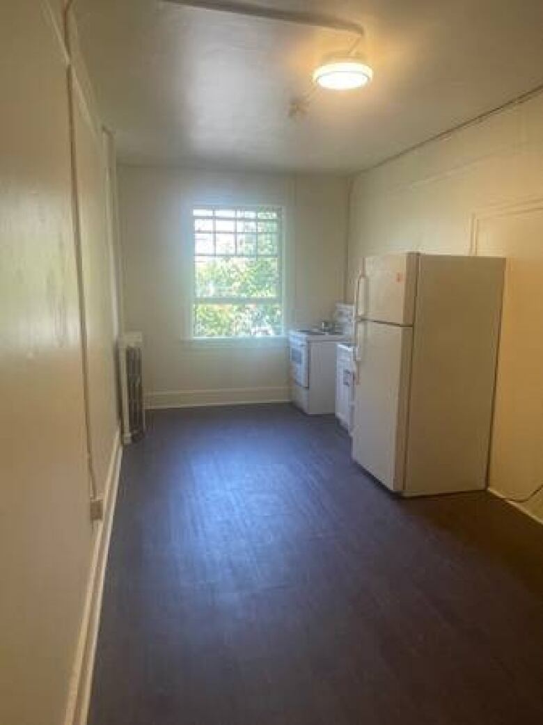 A bare room with a fridge, stove, and window.