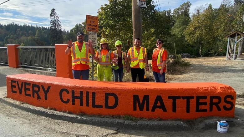 A group of people in high-vis vests stand over a barricade reading 'Every Child Matters'.