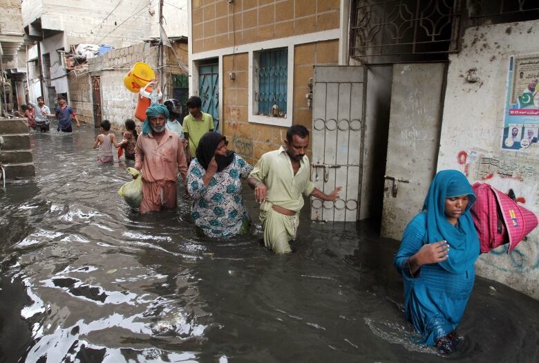 People are shown wading through waist-high water during the flooding this summer in Pakistan.