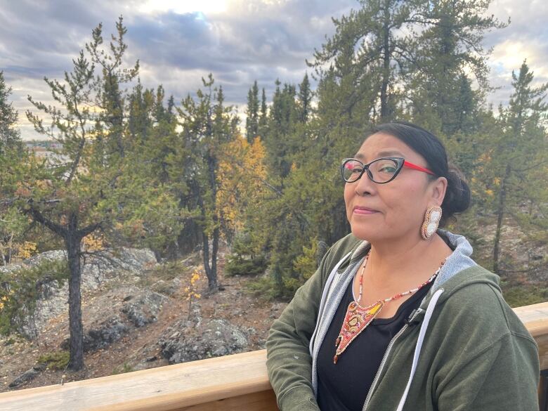 Smiling woman wearing beaded earrings near forest.