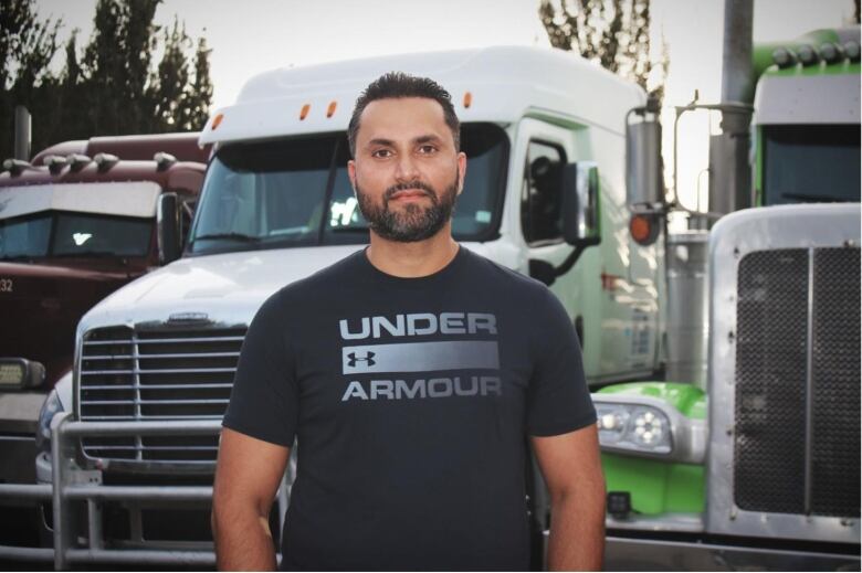 A South Asian man with a black t-shirt stands in front of a truck.