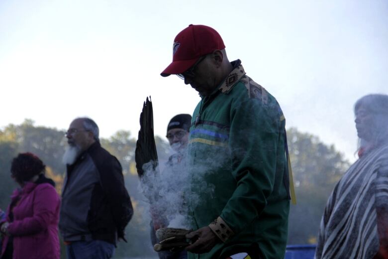 A man holding an eagle feather fans tobacco burning in a small bowl.