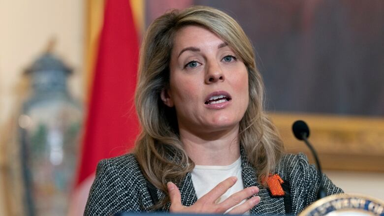 A woman in a grey jacket stands at a podium.