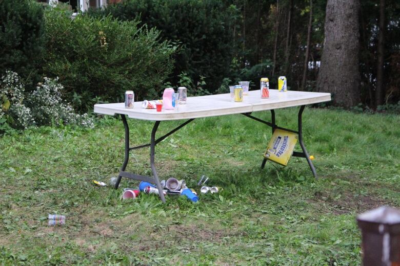 A white, collapsible table with empty cans and plastic cups on top and under it. 