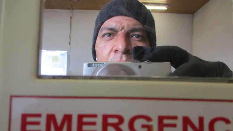 A man takes a photo into a mirror with an Emergency Eyewash Station sign below it.