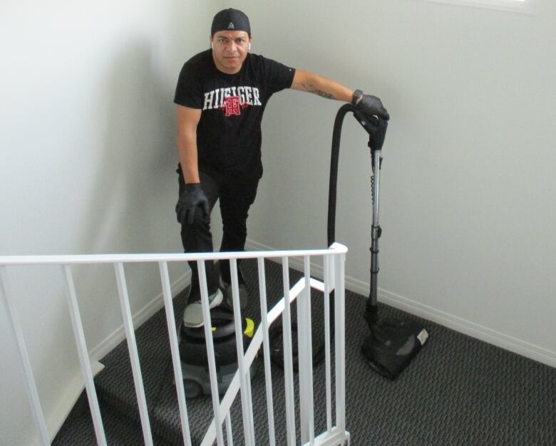 A man stands with a vacuum cleaner in a stairwell. 