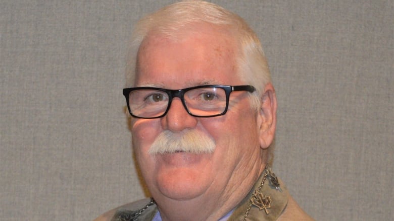 A man with white hair and a white mustache wearing black rimmed glasses