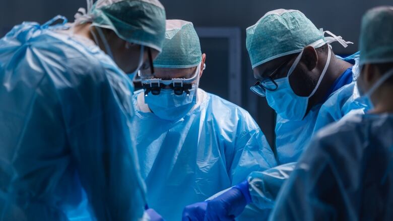 A group of doctors stand around ready to perform surgery.