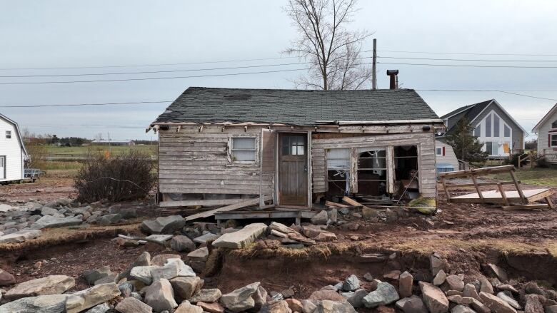 A small house, damaged by a storm, sits on a muddy lot.