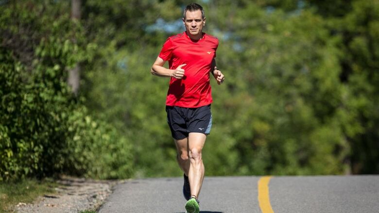 A man in a red shirt runs down a path on a sunny day.