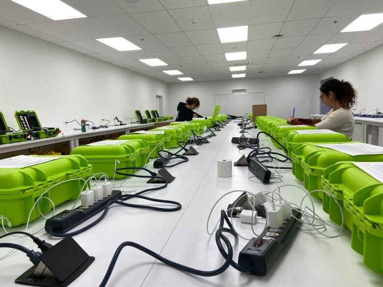 Two women work over two rows of bright green boxes.