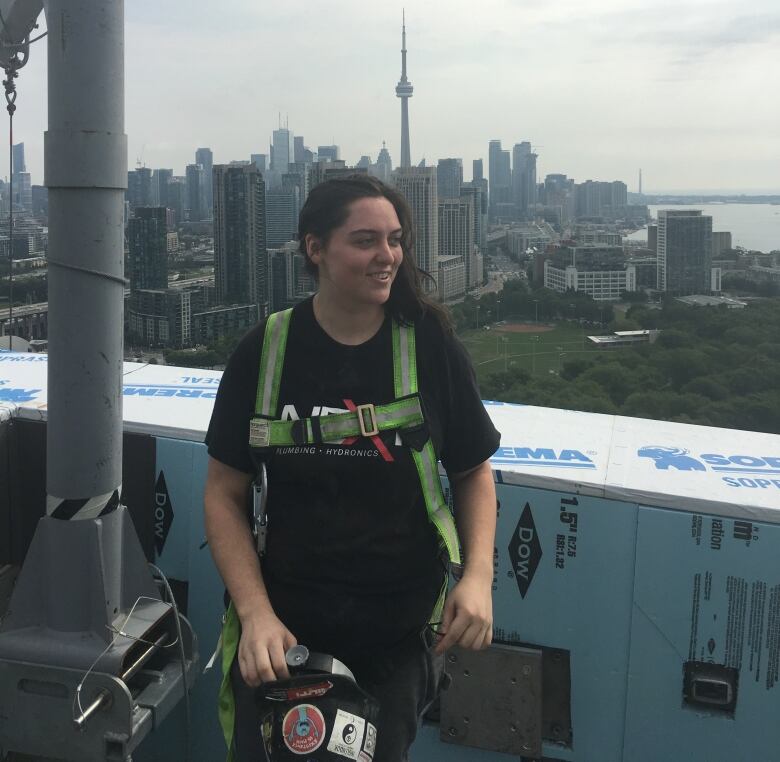 Woman wears green chest harness while standing on a roof overlooking Toronto.