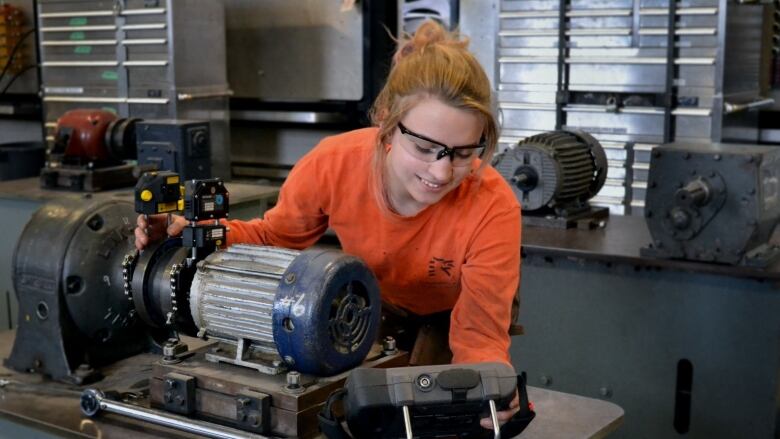 Woman wearing safety goggles works over machinery.