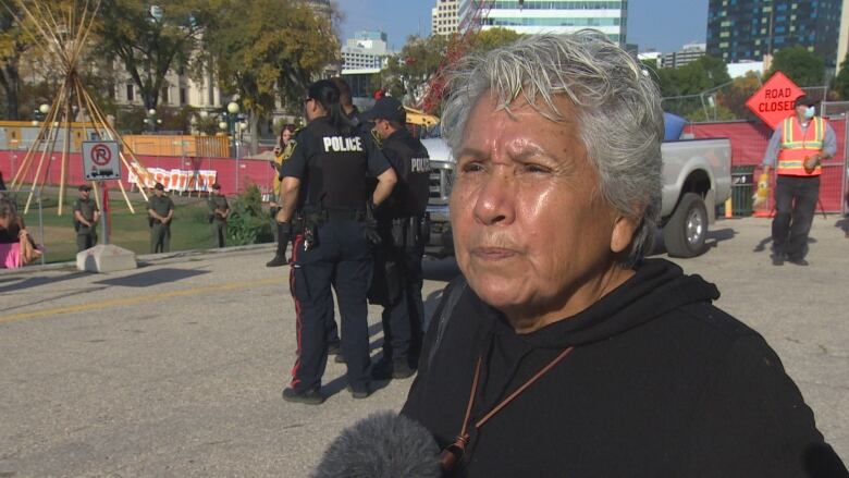 A woman with grey hair stands with pursed lips in front of the encampment as it's being dismantled.