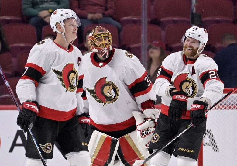 Two skaters and a goalie smile on the ice after a game.