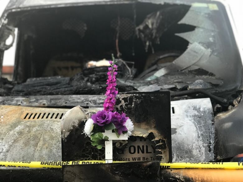 A cross and flowers is seen hung to a destroyed vehicle.