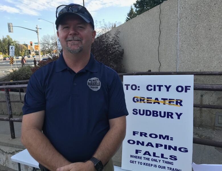 Man wearing ball cap stands beside protest sign