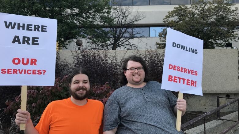 Two men stand side-by-side holding protest signs.