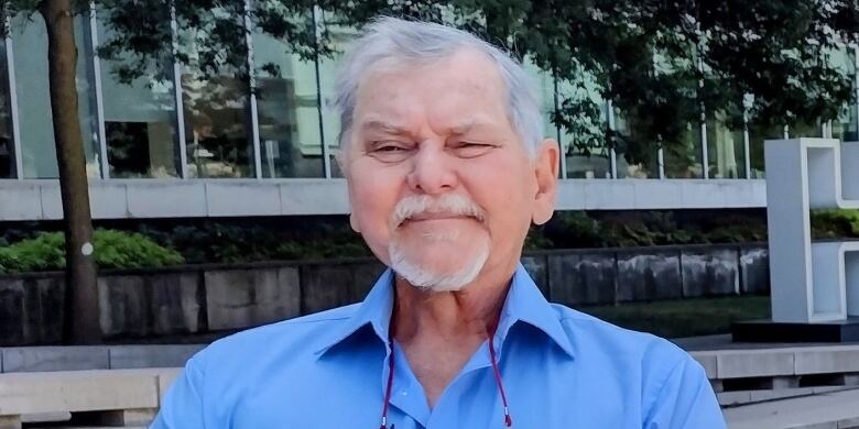 A man looks at the camera. He has a blue shirt on and is in front of Hamilton city hall.