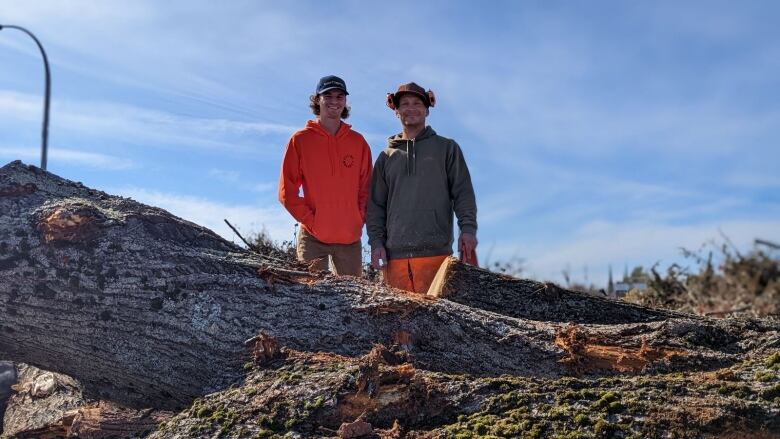 Two men stand next to a tree on the ground 