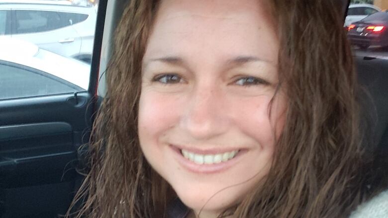 A closely cropped shot of a woman's face. She has long brown hair and appears to be sitting in a car.