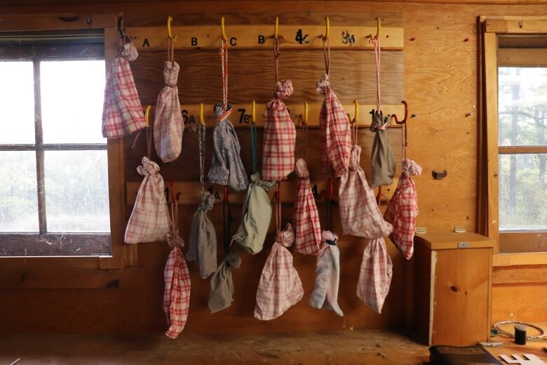 Bags hang on hooks against the inside wall of a wooden shed. There are live birds in each bag, waiting to be tagged. 