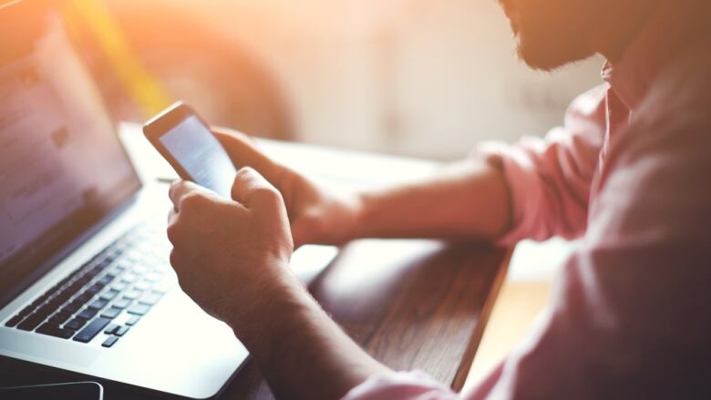 Man holding phone sitting at a table with a laptop.