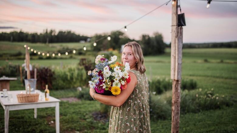 A woman stands in a field holding a massive bouquet of flowers.