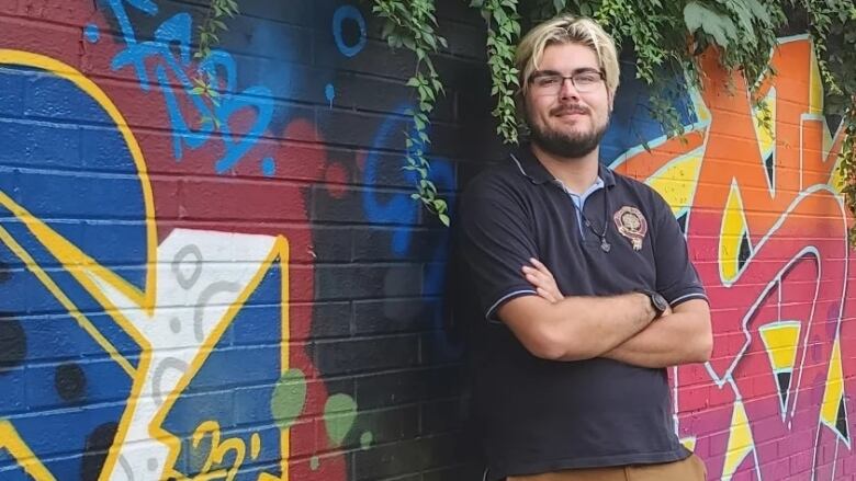 A young man stands in front of a wall with a mural on it.