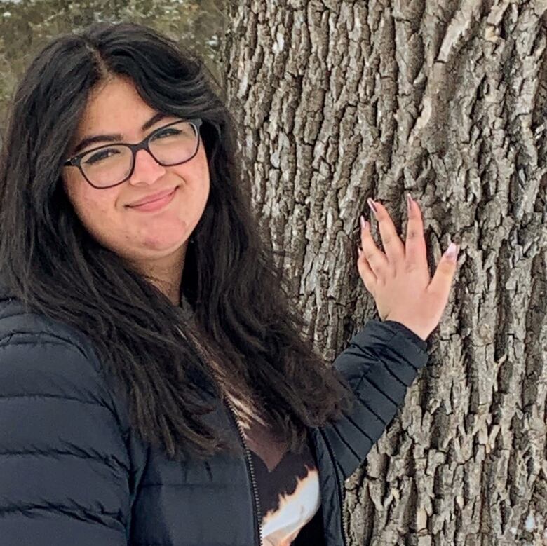 A young woman standing next to a tree.