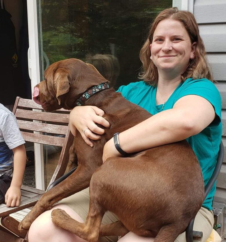 A woman holds her large dog on her lap.