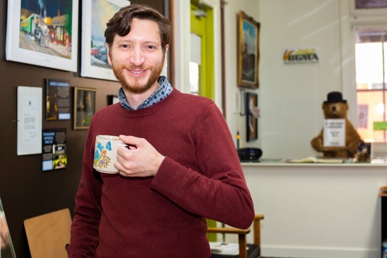 A man stands smiling and holding a tea cup.