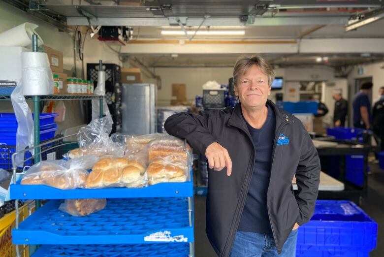 Man leans on a blue shelf filled with bags of hamburger buns